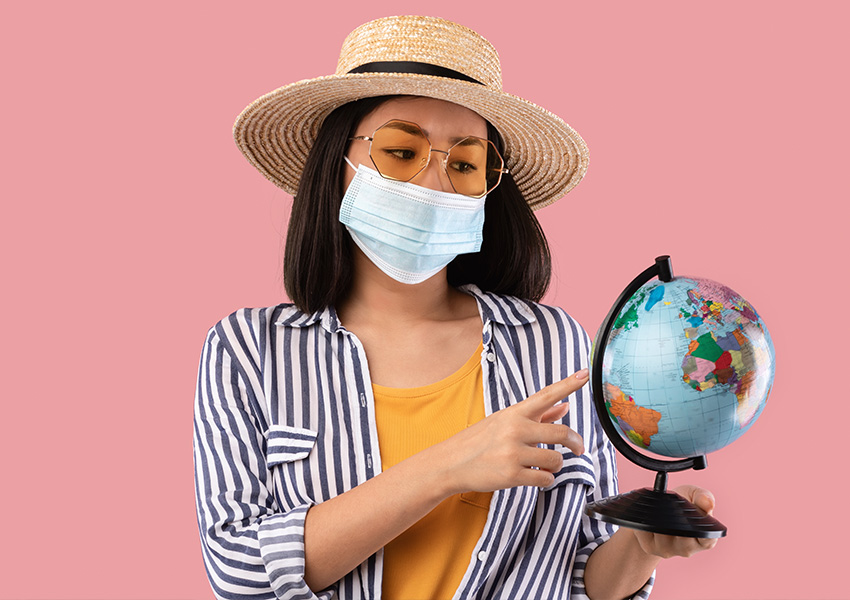 Woman wearing a face mask and straw hat pointing at a globe, representing travel vaccinations in Manchester