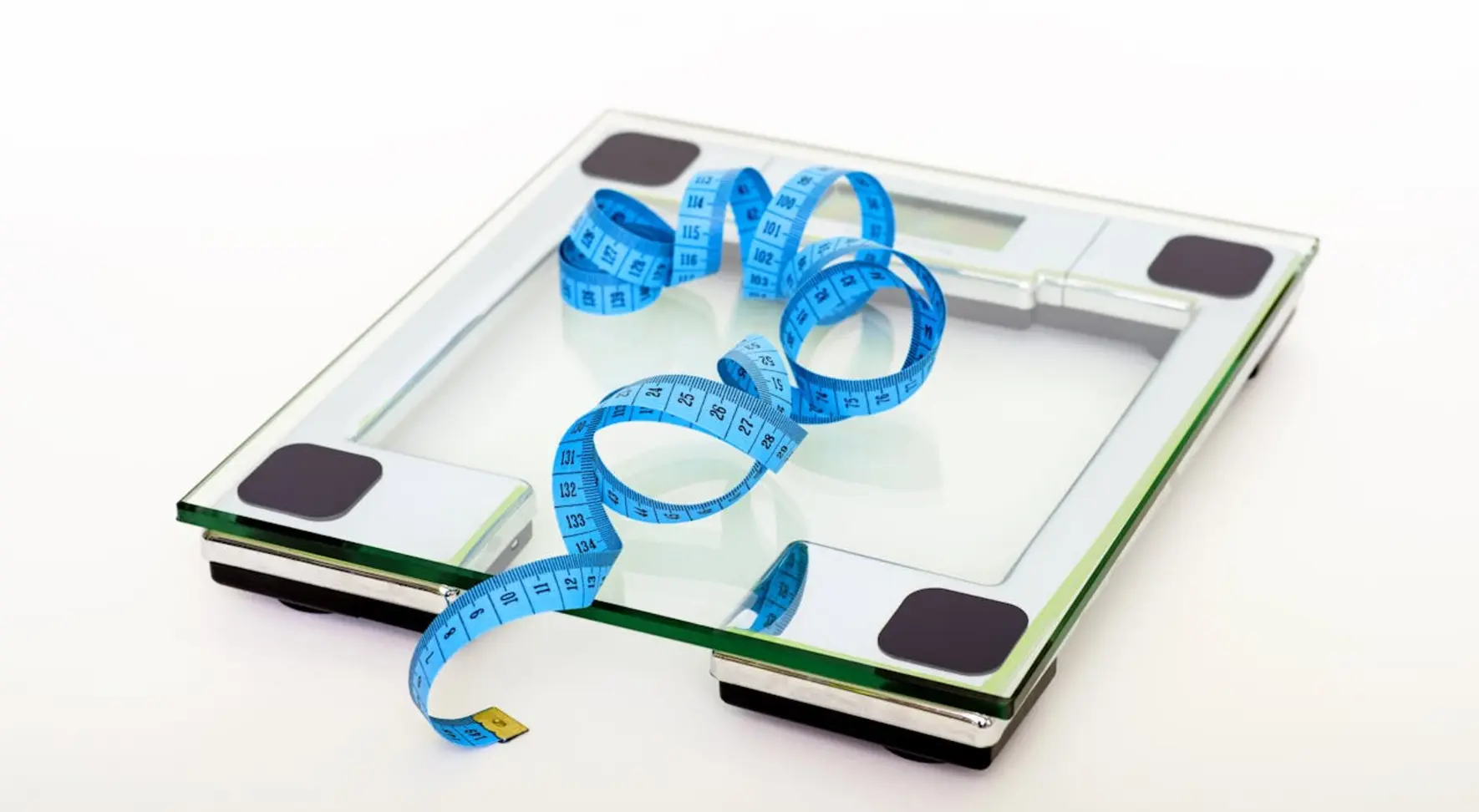 A digital bathroom scale with a blue measuring tape draped across its glass platform on a white background